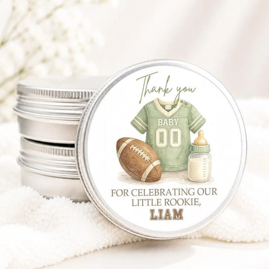 A round tin lid with a graphic design featuring a football jersey, baby bottle, and a ribbon, along with the text "Thank you for celebrating our little Rookie, Liam".