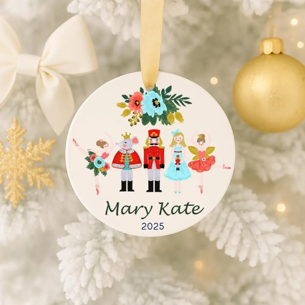 A round ornament hanging on a Christmas tree, featuring a nutcracker, a ballerina, and other characters, with a gold ornament and snowflakes in the background.
