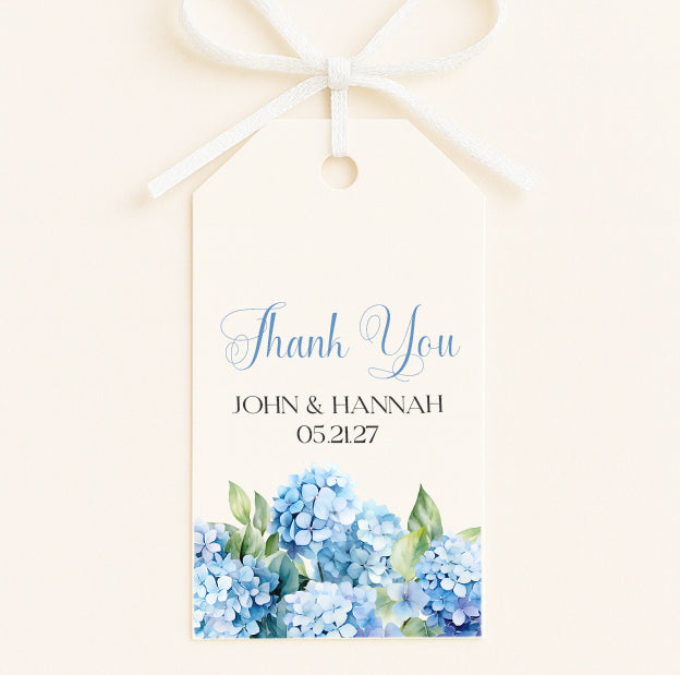 A white tag with a bow, featuring a blue watercolor illustration of blue hydrangeas and the text "Thank You John & Hannah 05/27".