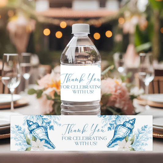 Coastal seashell water bottle labels with blue botanical artwork displayed at an elegant seaside-inspired table setting.