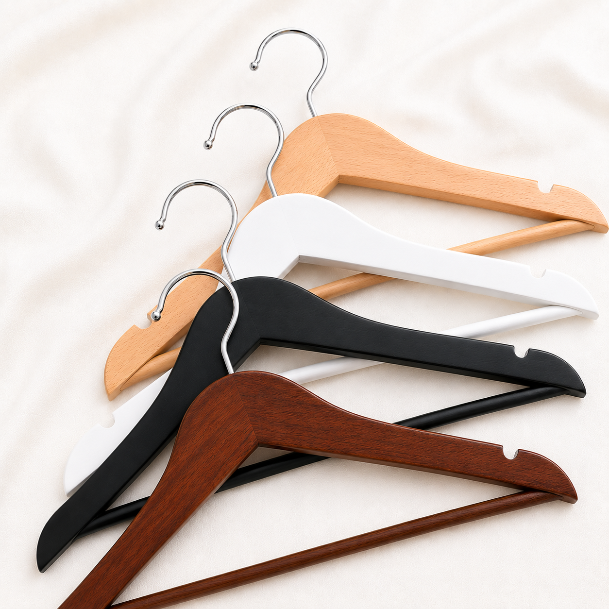 Four wooden hanger color options displayed on a soft ivory fabric background, featuring natural wood, white, black, and walnut finishes with silver metal hooks. Perfect for personalized wedding dress hangers, bridesmaid gifts, and custom engraved keepsakes.