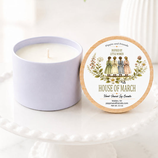 a hand-poured soy candle sits on a white scalloped pedestal beside its matching wooden lid. The lid features a Little Women–inspired label with a vintage watercolor illustration of the four March sisters standing together, framed by delicate wildflowers. The label reads "Inspired by Little Women – House of March" with "Hand-Poured Soy Candle" below. The candle is styled on a bright marble surface with a softly blurred white vase of flowers in the background, creating a warm look