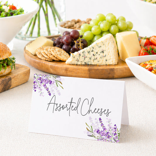 Lavender food tent cards with purple floral design displayed on table labeling dishes for wedding or bridal shower buffet.