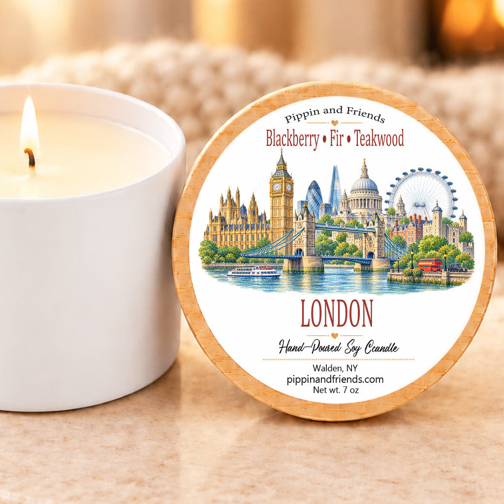 A round wooden-lidded candle tin labeled London with an illustrated cityscape and text 'Blackberry • Fir • Teakwood' sits beside a lit white candle on a beige stone surface in a warm indoor setting.