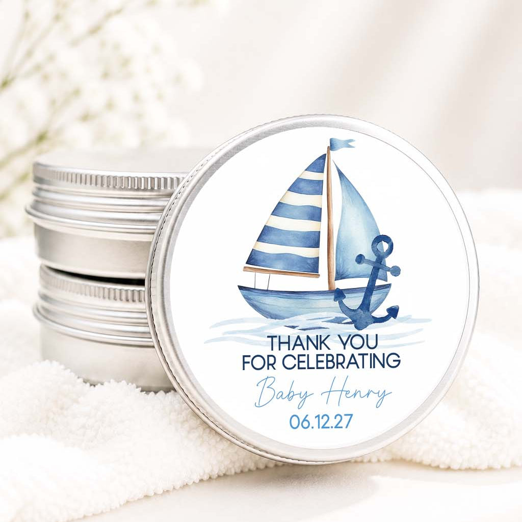 A stack of round silver metal tins with one tin shown from the front, featuring a nautical-themed baby shower favor label with a blue and white striped sailboat, anchor, and the text 'THANK YOU FOR CELEBRATING Baby Henry 06.12.