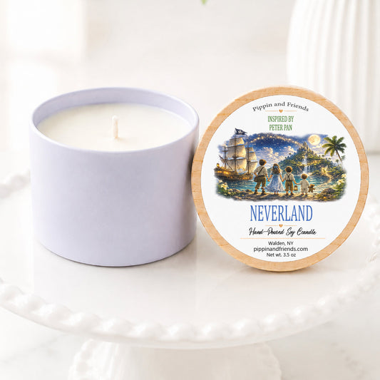 A soycandle jar sits beside its round lid on a white pedestal. The lid features a scenic illustration labeled 'NEVERLAND' with a ship, palm trees, and the text 'Pippin and Friends' and 'Inspired by Peter Pan'.