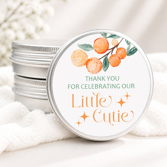 Little Cutie baby shower candle favor in a silver tin featuring watercolor oranges, greenery, and a sweet citrus-themed design displayed on a wooden surface.
