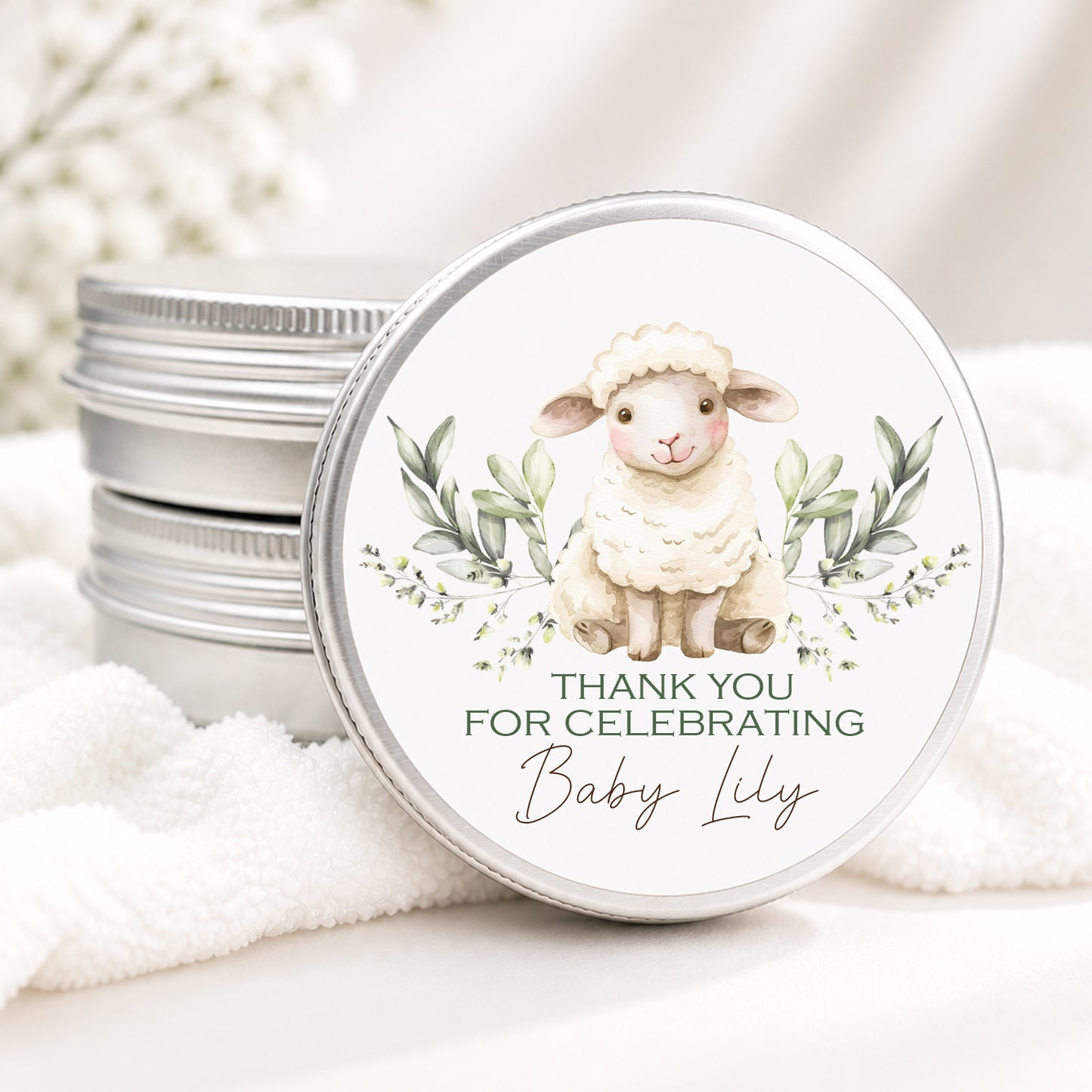 Personalized lamb baby shower candle favor in a silver tin featuring a watercolor sheep and greenery design on a wooden surface.