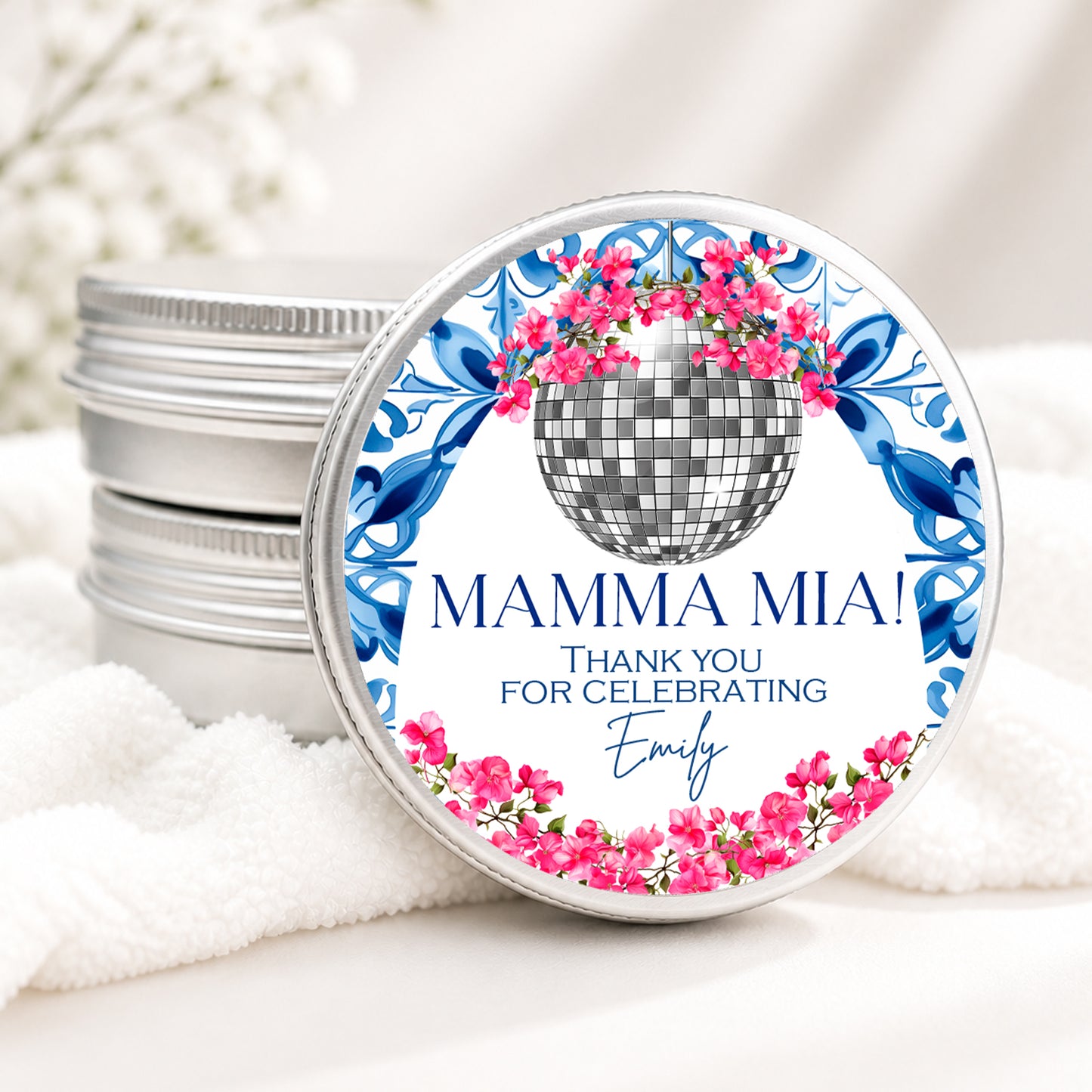 Personalized Mamma Mia themed candle favor in a silver tin featuring a disco ball, pink bougainvillea flowers, blue Mediterranean tile design, and custom event details on a soft white background.