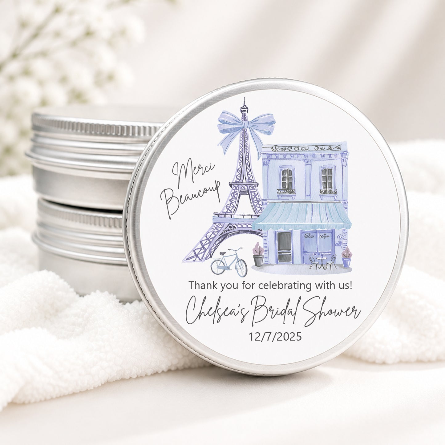 Personalized Paris bridal shower candle favor in a silver tin featuring a watercolor Eiffel Tower, Paris café storefront, and custom event details, displayed on a soft white background.