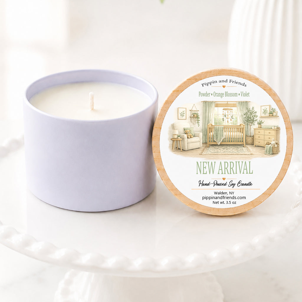 A soy candle in a white ceramic vessel with a natural wood lid featuring a watercolor baby nursery label, hand-poured by Pippin and Friends