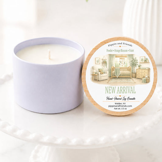 A soy candle in a white ceramic vessel with a natural wood lid featuring a watercolor baby nursery label, hand-poured by Pippin and Friends