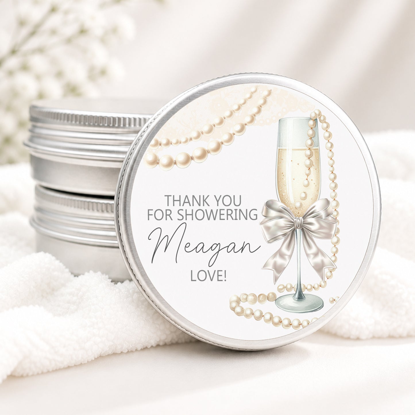 Personalized bridal shower candle favor in a silver tin featuring a champagne flute with a satin bow, elegant pearl accents, and custom event details, displayed on a soft white background.