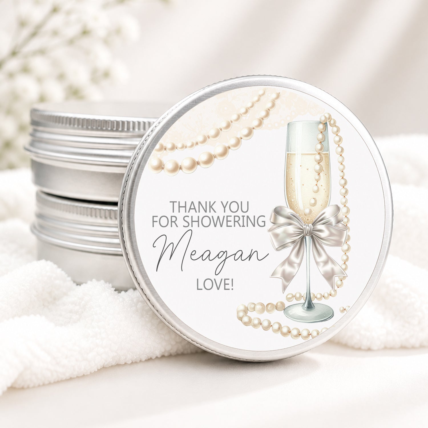 Personalized bridal shower candle favor in a silver tin featuring a champagne flute with a satin bow, elegant pearl accents, and custom event details, displayed on a soft white background.