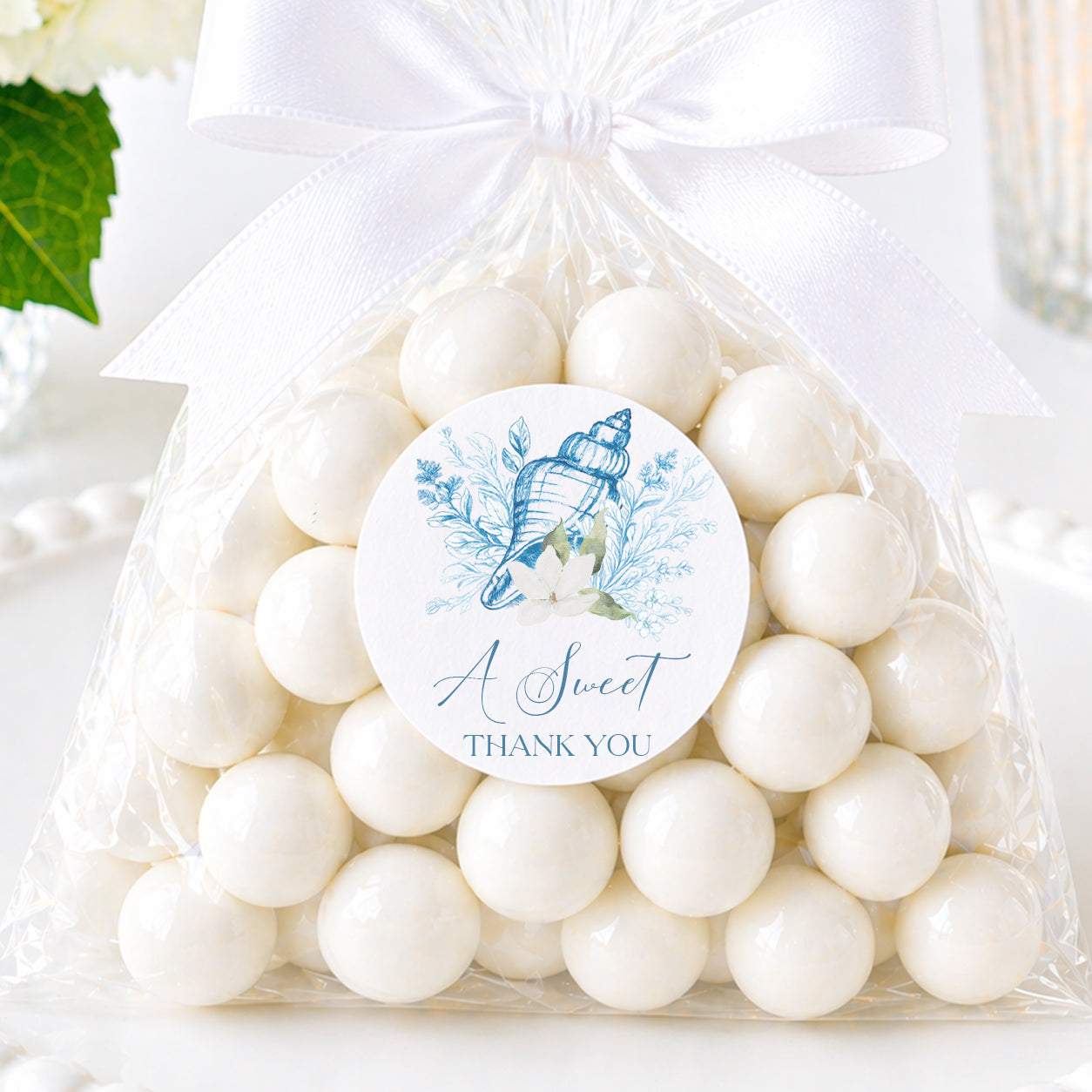 Coastal seashell favor sticker with “A Sweet Thank You” wording displayed on a candy favor bag with white satin ribbon for bridal showers and beach weddings.