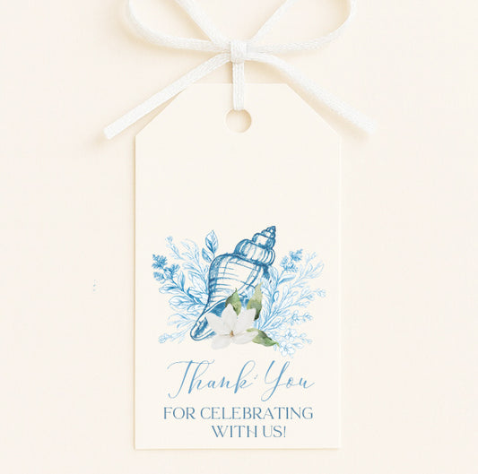 A white tag with a bow, featuring a blue and white seashell and flowers, along with the text "Thank You for Celebrating With Us!"