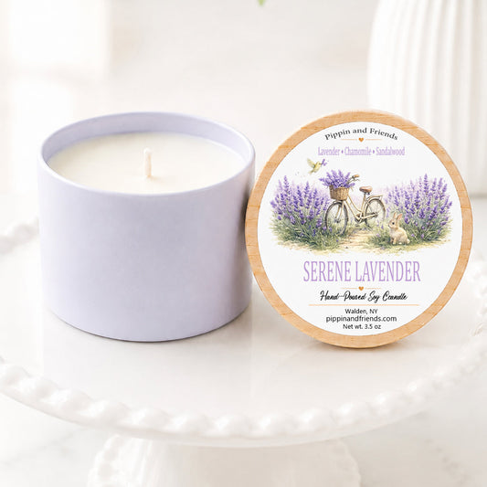 Serene lavender hand-poured soy candle in a matte white vessel with natural wooden lid displayed upright beside it, featuring a watercolor lavender field label. The candle sits on a white scalloped pedestal against a bright, airy background with soft white flowers in a vase, creating a clean, cozy aesthetic.