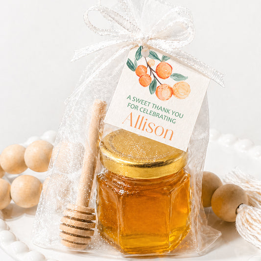 Cutie themed baby shower honey favor kit with orange design tag, mini jar, gold lid, wooden dipper, and sheer bag