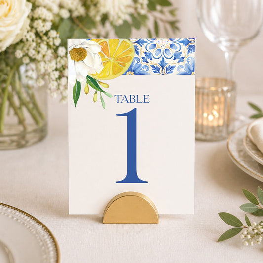Mediterranean lemon table number card with blue tile design displayed in gold stand on elegant wedding table setting.