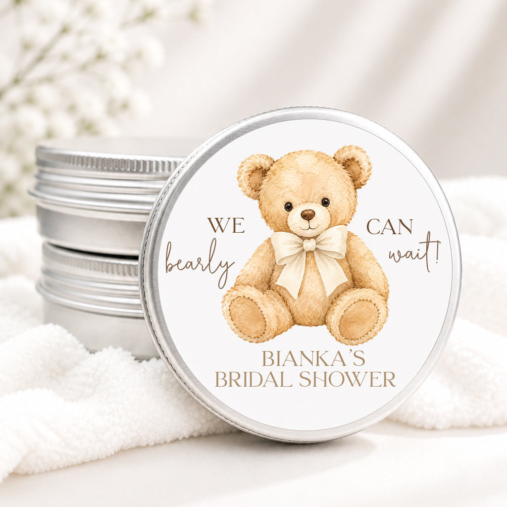 A round silver metal tin with a custom printed lid featuring a watercolor teddy bear and the text 'WE can wait! BIANKA'S BRIDAL SHOWER', shown next to stacked matching tins on a soft white fabric surface.