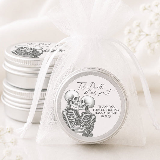 A small round silver favor tin sealed in a sheer white organza bag, with a printed skeleton illustration and the text 'The Death of us part' and 'THANK YOU FOR CELEBRATING JANNAMI & ERIC 8.2.