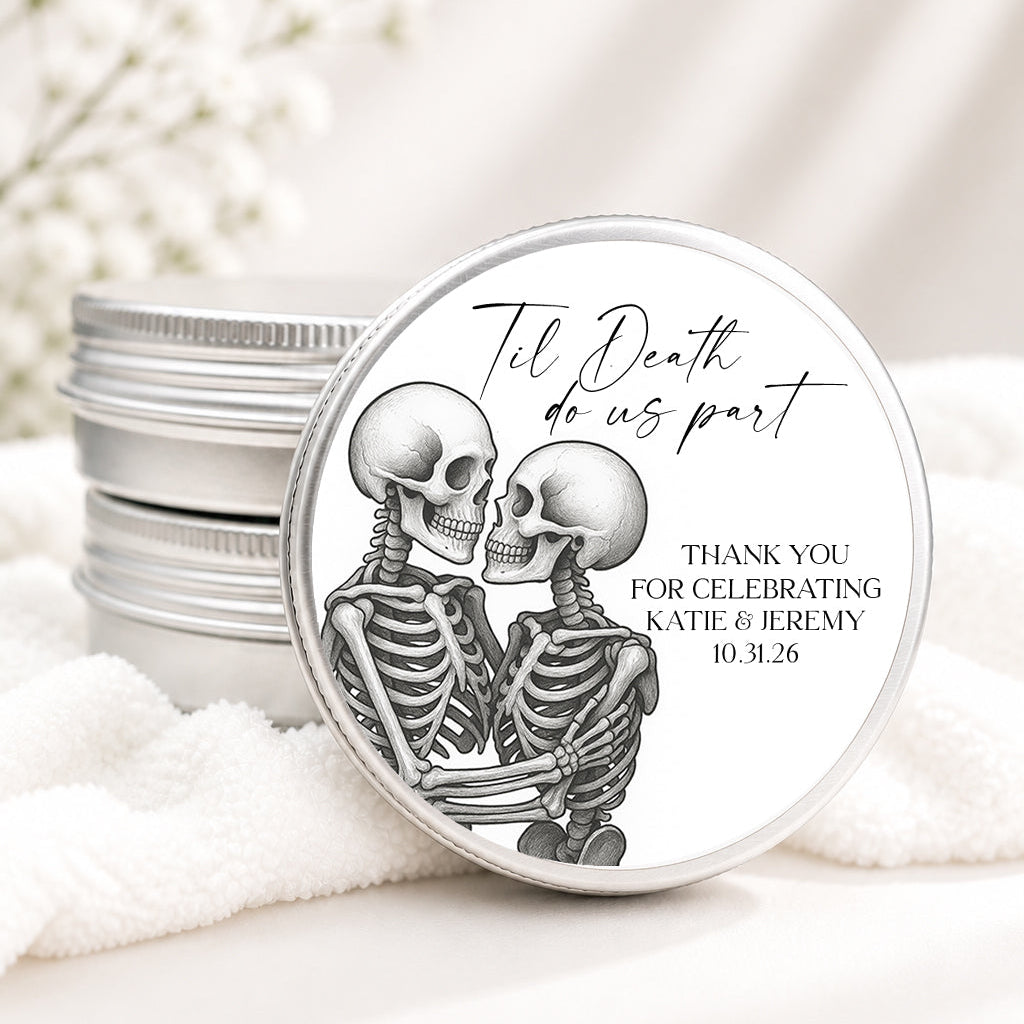 Round silver metal tins with a skeleton-themed wedding favor label reading 'Til Death do us part' and personalized thank you text, styled on white fabric with soft white flowers in the background.